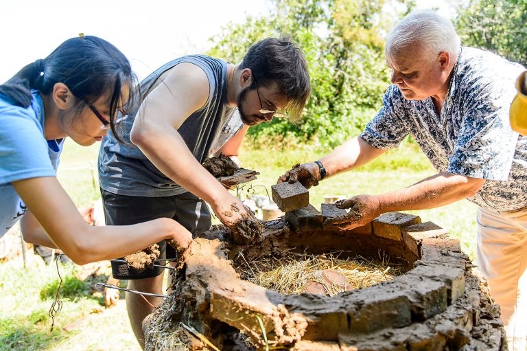 Graduate exchange student Ai Wanqiao (left) and Alan Lee (center) use mud and bricks to build a cap for a kiln